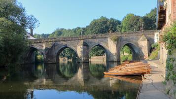 A stone bridge over a calm river with a wooden boat docked on the right.