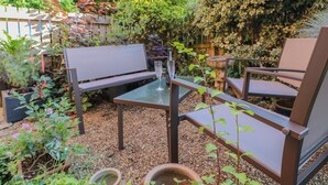 Une terrasse avec une table en verre, deux chaises et un banc.