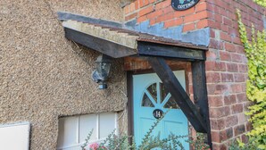 Une petite maison en briques avec une porte bleue, une plaque portant le numéro 14 et une autre plaque indiquant « Rosewood Cottage ».