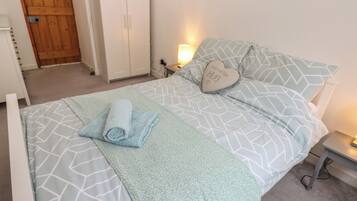 A neatly made bed with patterned bedding, a heart-shaped pillow, and a rolled towel on the bed.