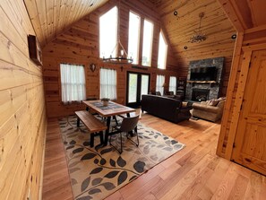 Interior d'una cabana de fusta amb taula de dinar, bancs, sofà i llar de foc.