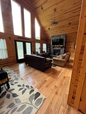 A spacious living room with a fireplace, a television, and a large window. - GORGEOUS LAKE FRONT CABIN - PRIVATE LAKE ACCESS-FISHING, KAYAKING, AND HIKING. (Topton)