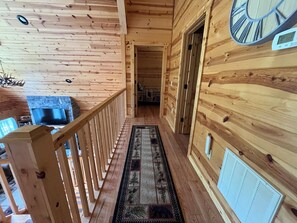 A wooden interior with a wooden railing, a rug, and a wall-mounted clock.