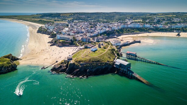 An aerial view of a coastal town with a beach, a fortified structure, and a pier.