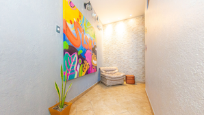 Un pasillo estrecho con un mural colorido en la pared izquierda, una planta en maceta, un banco acolchado y una cesta de mimbre.