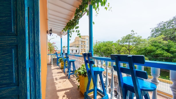 Balcón con sillas azules y una maceta amarilla, con vistas a un paisaje urbano.