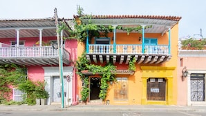 Un edificio de dos pisos con un balcón, una puerta con un letrero y una ventana con celosía decorativa.