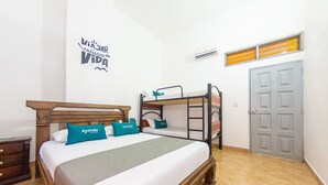 Un dormitorio con una cama nido, un cabecero de madera, una cama con almohadas turquesa, una manta gris, una mesita de noche de madera, un aparador y una puerta gris.