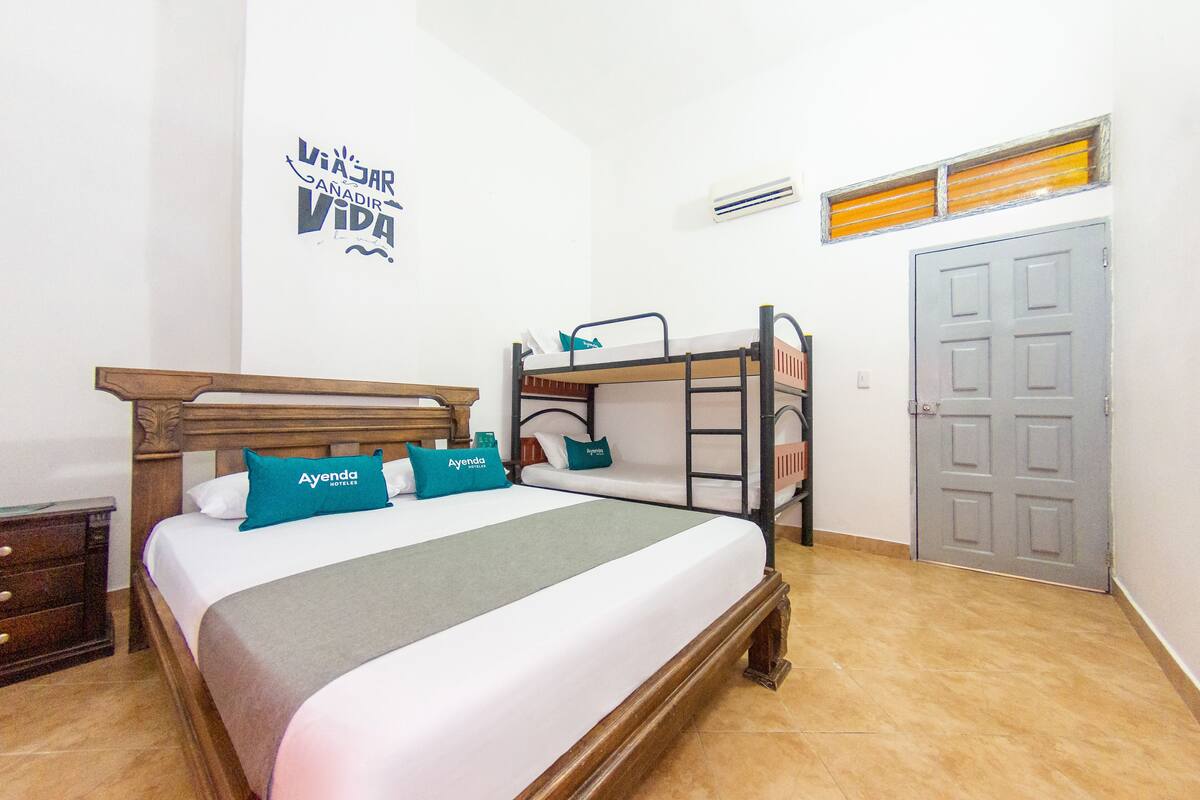 A bedroom with a bunk bed, a wooden headboard, a bed with teal pillows, a grey blanket, a wooden nightstand, a dresser, and a grey door.