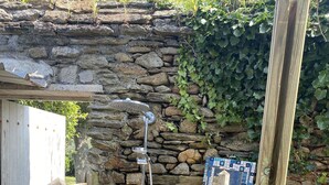 Un espace de douche aux murs en pierre, doté d’un flexible et d’un pommeau de douche en métal, d’une porte en bois et d’une décoration en mosaïque.