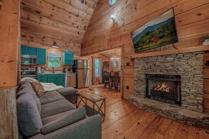 Ein gemĂŒtliches Blockhaus-Interieur mit Kamin aus Stein, Holzböden, einer Couch und einer KĂŒchenzeile.