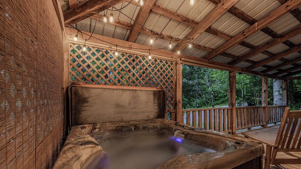 Uma banheira de hidromassagem sob uma pérgola de madeira com um painel treliçado e luzes de corda.