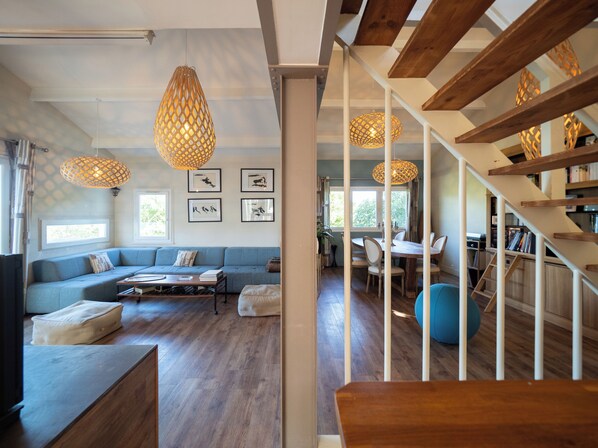 A modern living room with a blue sofa, wooden flooring, and a staircase with wooden railings. - Villa with magnificent unoverlooked sea view - 150m2 (Veulettes-sur-Mer)