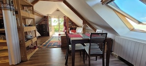 A cozy attic room with a dining table, chairs, and a view through a skylight.