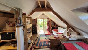 Une chambre mansardée chaleureuse, avec un lit en mezzanine, un bureau en bois, une petite table et une fenêtre avec des rideaux.