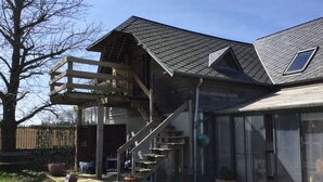 Une maison à deux étages avec une terrasse en bois, un escalier et une grande fenêtre.