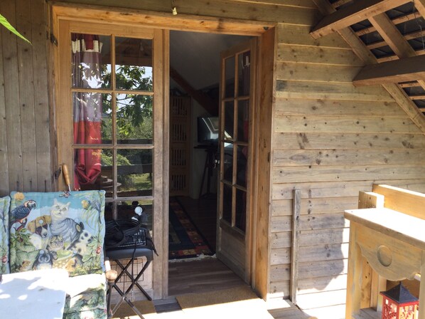 A wooden cabin with a large open door leading to a hallway. There is a small table with a colorful cloth and a chair.