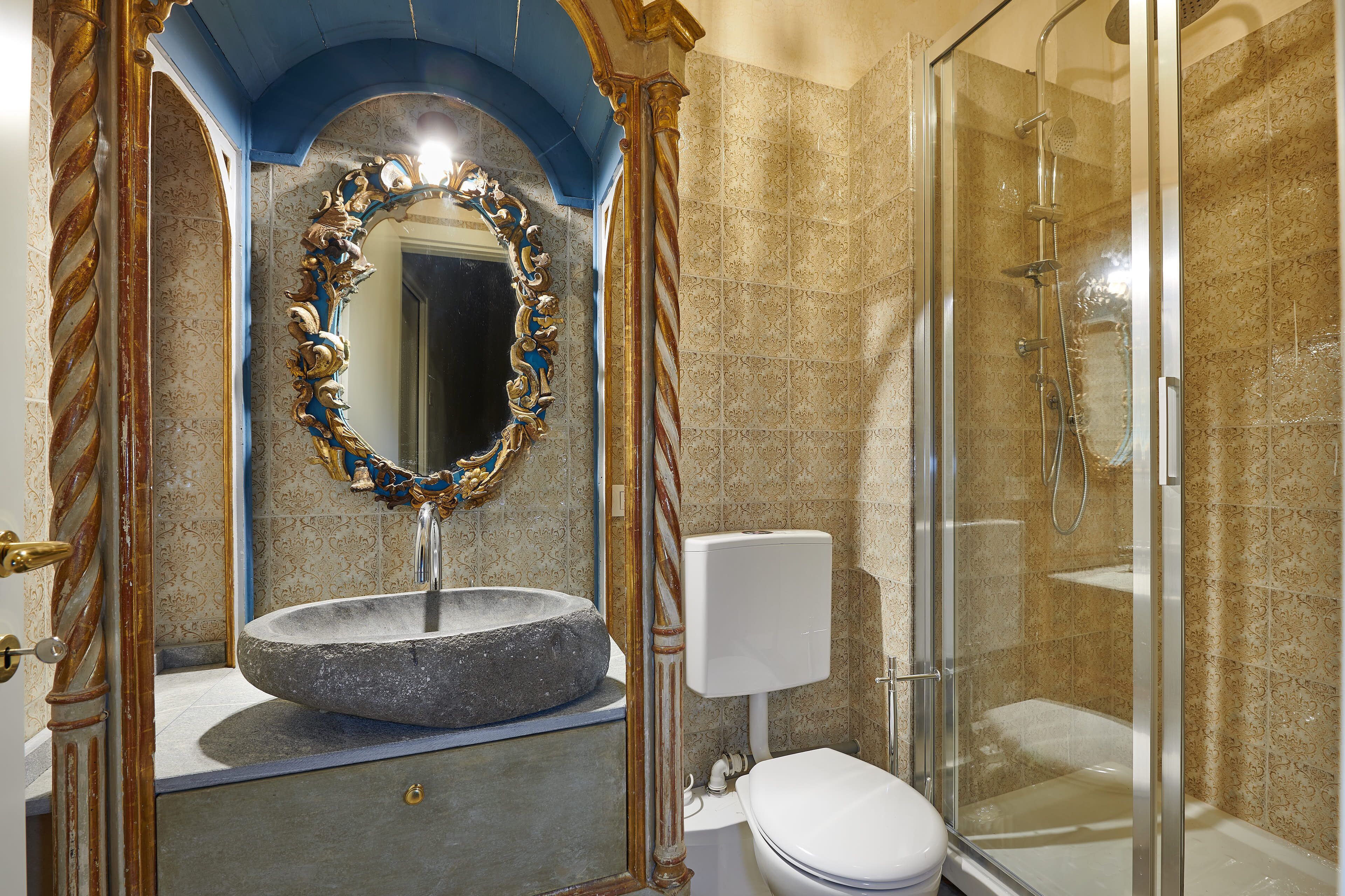 Une salle de bain avec un lavabo en pierre, des toilettes blanches et une douche à parois de verre.