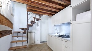 Una cocina con armarios blancos, estufa a gas y una escalera de madera.