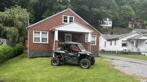 Une maison en briques rouges, avec un porche blanc et un véhicule tout-terrain Polaris garé devant.