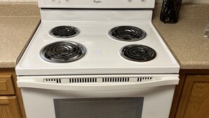 Une cuisinière Whirlpool blanche, dotée de quatre brûleurs, d’une horloge numérique et d’une pancarte au-dessus indiquant : « JE VEUX TOUT, ET JE VEUX QUE CE SOIT LIVRÉ ! ».