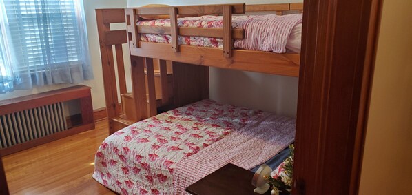 Ein Stockbett mit Holzrahmen und einem unterem Bett mit blumigem Überwurf.