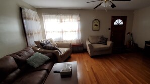 Un salon avec un canapé en cuir marron, deux fauteuils, une table basse et un ventilateur de plafond.