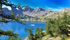 A mountainous landscape with a clear lake, surrounded by trees and rocky terrain. - Studio (Allos)