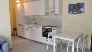 Una cuina compacta amb armaris blancs, un rentaplat i una zona de dinar amb taula i cadires.