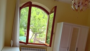 Un dormitori amb un llit, un radiador, una finestra amb cortines, un armari i una làmpada penjant.
