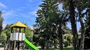 Un parc infantil amb tobogan i un petit refugi, envoltat d'arbres i gespa.