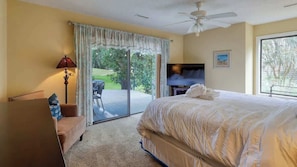 A bedroom with a bed, a TV, a ceiling fan, a couch, and a sliding glass door to a balcony. - Beautiful Villa! Beach, Golf, Tennis Hilton Head (Hilton Head Island)
