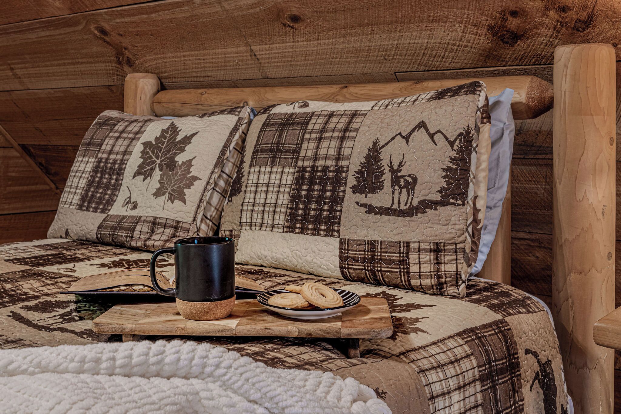 A cozy room with a wooden headboard, a quilted bedspread, a mug, and a plate of cookies.