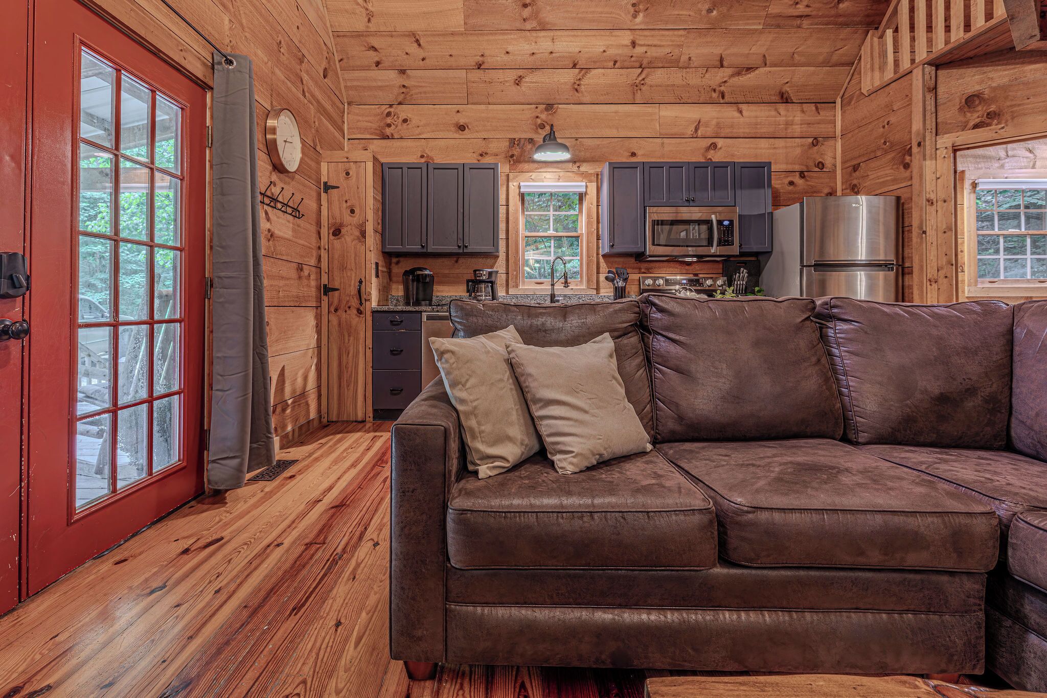Ein Holzblockhaus-Interieur mit einer braunen Ledersofa, einer Küchenzeile und einer roten Tür.
