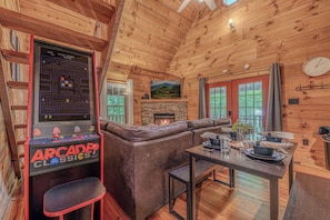 A cozy cabin interior with a wooden ceiling, a fireplace, a sofa, and an arcade game. - Woodland Cabin Near Cades Cove, Hot Tub, Arcade (Townsend)