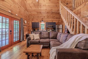 A wooden interior with a brown leather couch, a wooden coffee table, and a staircase.