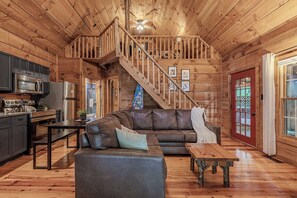 A wooden cabin interior with a kitchen, dining area, and a staircase.
