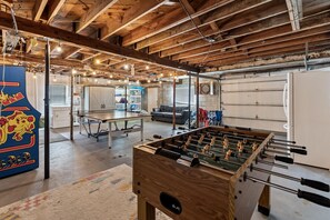 A spacious room with a foosball table, a ping pong table, and a dartboard.