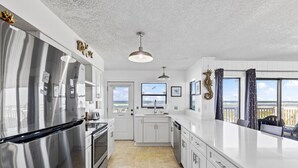 A modern kitchen with stainless steel appliances, white cabinetry, and a view of the ocean. - Tipsy Turtle & Funky Pelican Massive Oceanfront (Palm Coast)