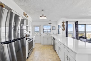 A modern kitchen with stainless steel appliances, white cabinetry, and a view of the ocean through large windows.