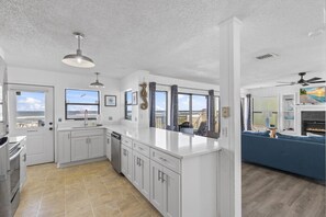 A modern kitchen with white cabinets, a large island, and a view of the ocean.