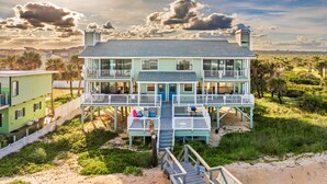 A two-story beachfront house with a balcony, a deck, and a sandy beach in the background. - Tipsy Turtle & Funky Pelican Massive Oceanfront (Palm Coast)