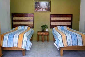 A room with two beds, a small table with a plant, and a framed picture on the wall.