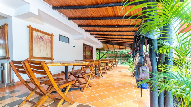 A covered outdoor dining area with wooden tables and chairs, a tiled floor, and a view of greenery. - Hotel Casa Baquero (Villavicencio)