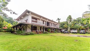A two-story building with a balcony, surrounded by lush greenery and parked vehicles. - Hotel Casa Baquero (Villavicencio)