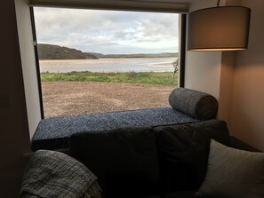 Ein Zimmer mit Blick auf den Strand, ein Fenster, eine Lampe und eine Bank.