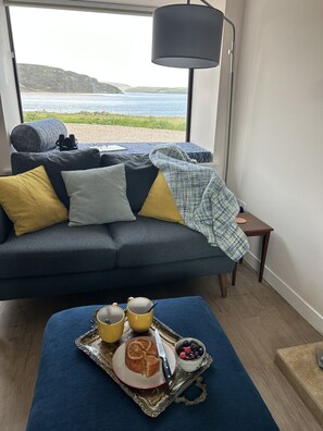 Ein gemütliches Zimmer mit einer Couch, einem Tablett mit Frühstück und Blick aufs Meer.