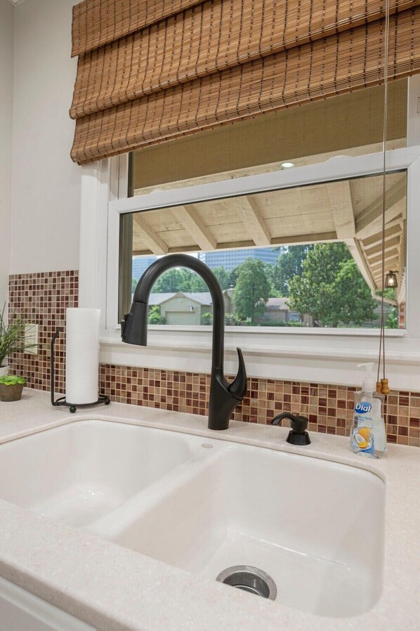 A kitchen with a double sink, a window with a view of trees and houses, a potted plant, and a bottle of Dial dish soap. - Southern Hills Stunner! 3bd/2bth (Tulsa)