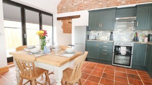 Een keuken met groene kastjes, een betegelde vloer en een eettafel met stoelen.