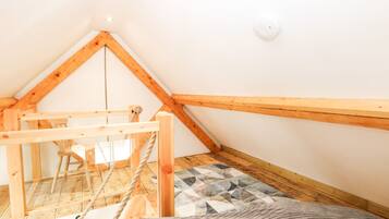 Un pequeño cuarto ático con techo inclinado, vigas de madera, una escalera de cuerda y una alfombra estampada.